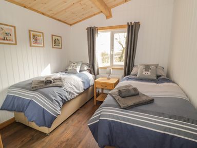 A bedroom with two single beds with folded towels on them a wooden nightstand with a lamp a window with curtains and framed pictures on the wall at Top Style Orchard in Hallow