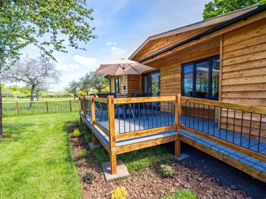 A wooden deck with outdoor chairs a table and an umbrella next to a wooden house at Top Style Orchard in Hallow