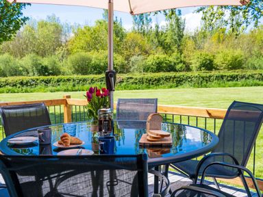 An outdoor glass table with croissants coffee mugs sliced bread and flowers under an umbrella at Top Style Orchard in Hallow