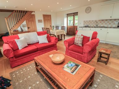 A living room with red furniture and a dining area at Bramble Cottage in Babcary near Lydford-On-Fosse