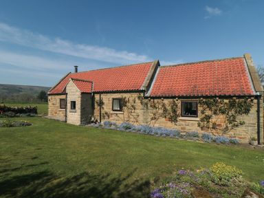 A stone house with red tiled roof surrounded by grassy lawn and flowers at Silver Birches in Glaisdale