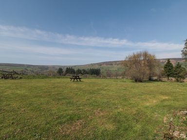 A grassy field with picnic tables trees and hills in the background at Silver Birches in Glaisdale