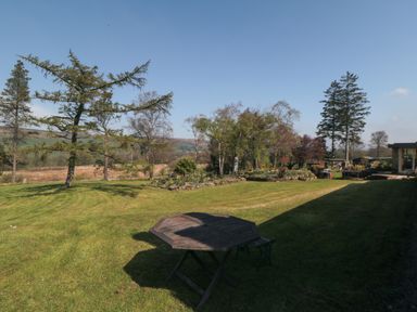 A garden with grass trees flowerbeds a wooden table and benches at Silver Birches in Glaisdale