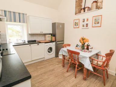 A kitchen with white cabinets a table with flowers and wooden chairs at Silver Birches in Glaisdale