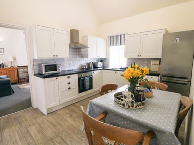 A kitchen with white cabinets black countertops a dining table with a blue polka dot tablecloth and yellow flowers at Silver Birches in Glaisdale