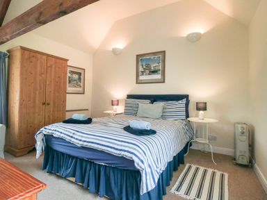 A bedroom with a double bed with striped bedding a wooden wardrobe two bedside tables with lamps and framed pictures on the walls at Silver Birches in Glaisdale
