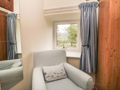 A small room with a light armchair next to a window with blue curtains and a wooden wardrobe at Silver Birches in Glaisdale