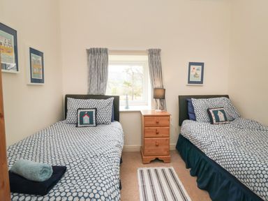 A bedroom with two single beds blue patterned bedding a wooden nightstand with a lamp and framed pictures on the walls at Silver Birches in Glaisdale