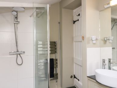 A bathroom with a glass shower enclosure a towel rack a white sink a mirror and a white paneled door at October Cottage in Chalford Gloucestershire