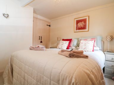A bedroom with a bed with pillows and folded towels bedside tables with lamps and a framed picture on the wall at October Cottage in Chalford Gloucestershire
