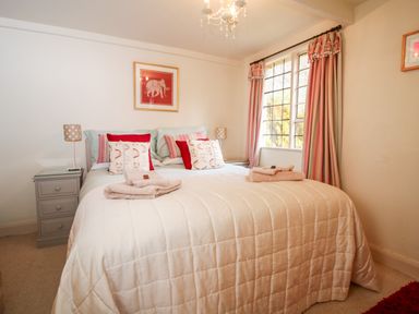 A bedroom with a double bed white bedding bedside tables with lamps and window with pink curtains at October Cottage in Chalford Gloucestershire