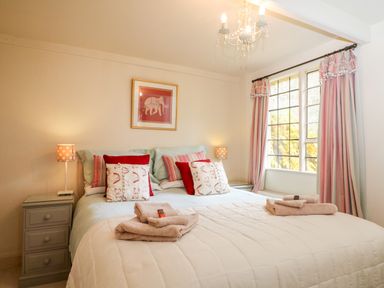 A bedroom with a double bed bedside tables lamps and a window with curtains at October Cottage in Chalford Gloucestershire