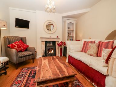 A living room with a striped armchair red cushions a wooden coffee table and a fireplace at October Cottage in Chalford Gloucestershire