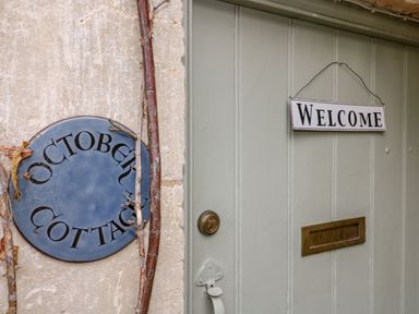 A door with a welcome sign a mail slot and a round sign saying October Cottage on a stone wall at October Cottage Chalford Gloucestershire