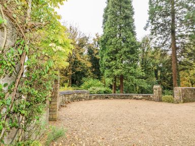 A gravel driveway with a stone wall and green trees at October Cottage in Chalford Gloucestershire