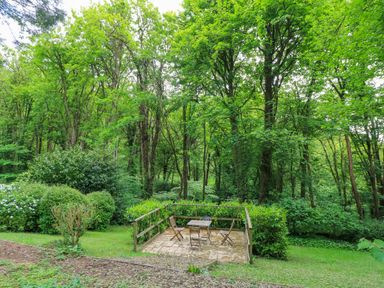 An outdoor patio with a table and four chairs surrounded by trees and bushes at October Cottage in Chalford Gloucestershire