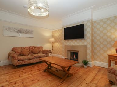 A living room with a sofa coffee table fireplace television and wooden floor at Greenlawns in Burnham-On-Sea