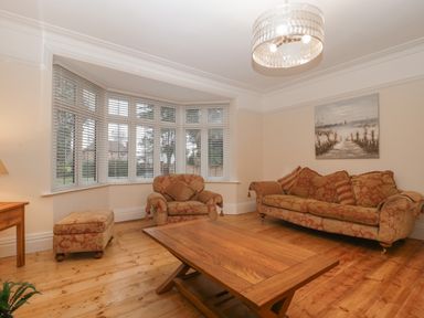 A living room with patterned sofa armchair ottoman wooden coffee table and large bay window at Greenlawns in Burnham-On-Sea