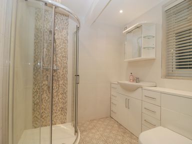 A bathroom with a corner shower enclosure a sink with cabinets a mirrored cabinet a window with blinds and a tiled floor at Greenlawns in Burnham-On-Sea