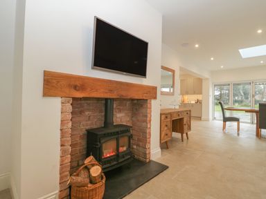 A room with a brick fireplace and wood burning stove and a wooden sideboard next to a dining table and chairs at Greenlawns in Burnham-On-Sea
