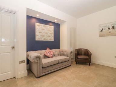 A sitting area with a beige sofa and a brown armchair against white walls at Greenlawns in Burnham-On-Sea