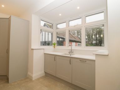 A kitchen corner with a sink under multiple windows and gray cabinets at Greenlawns in Burnham-On-Sea