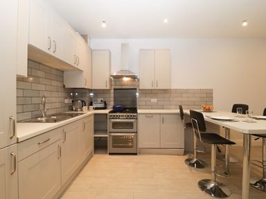 A kitchen with white cabinets a countertop stove sink kettle toaster and bar stools at Greenlawns in Burnham-On-Sea