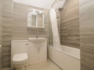 A bathroom with a toilet sink cabinet bathtub with shower and curtain at Greenlawns in Burnham-On-Sea