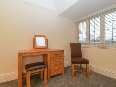 A room with a wooden dressing table mirror stool and a chair near a window with blinds at Greenlawns in Burnham-On-Sea