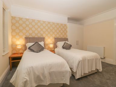 A bedroom with two single beds with gray pillows and white bedding bedside tables with lamps a radiator and wardrobe Greenlawns Burnham-On-Sea