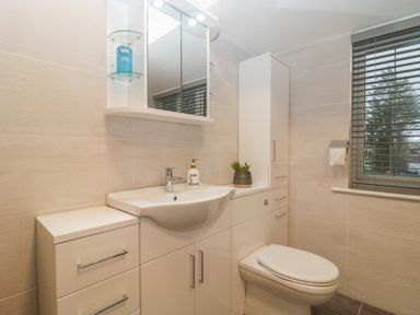 A bathroom with a sink, toilet, cabinet, mirror, and window with blinds at Greenlawns in Burnham-On-Sea