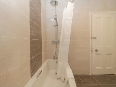 A bathroom with a bathtub shower combination and a white shower curtain partially closed at Greenlawns in Burnham-On-Sea