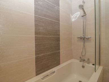 A bathroom with a bathtub shower combination and tiled walls at Greenlawns in Burnham-On-Sea