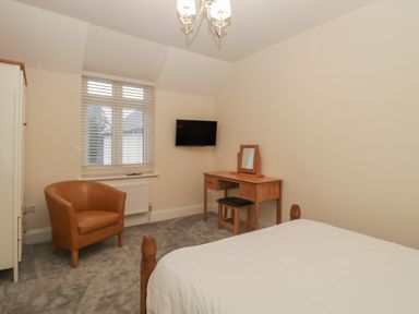 A bedroom with a wooden dressing table and stool a brown armchair a wall mounted television and a bed at Greenlawns in Burnham-On-Sea