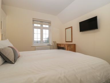 A bedroom with a bed pillows a wooden desk chair wall mounted tv and a window at Greenlawns Burnham-On-Sea
