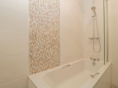 A bathtub with a showerhead and mosaic tile wall in a bathroom at Greenlawns in Burnham-On-Sea