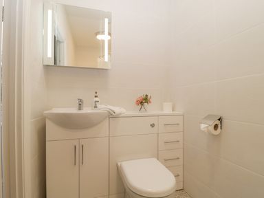 A bathroom with a white toilet sink cabinet mirror and toilet paper holder at Greenlawns in Burnham-On-Sea