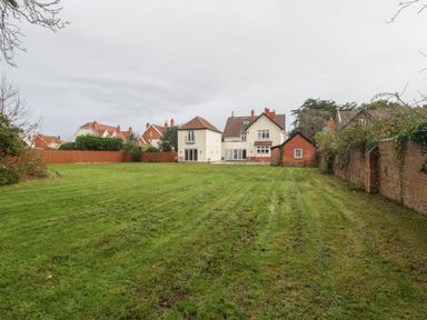 A large green lawn with houses and a brick wall surrounding the garden at Greenlawns in Burnham-On-Sea