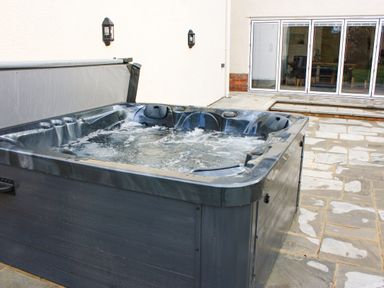 An outdoor hot tub with bubbling water on a stone patio next to a building with glass doors at Greenlawns in Burnham-On-Sea
