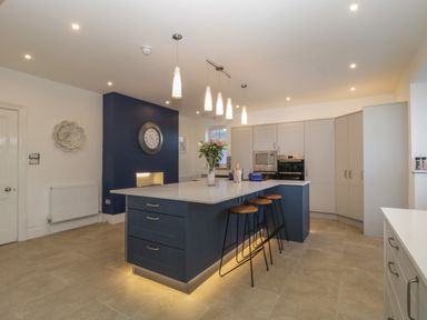 A kitchen with a large island with bar stools and a clock on a blue accent wall at Greenlawns in Burnham-On-Sea