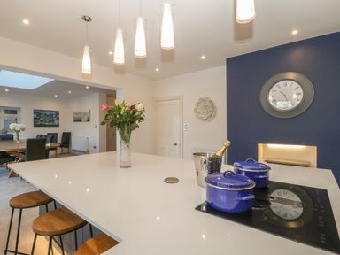 A kitchen island with stools pendant lights and blue pots on the stove at Greenlawns in Burnham-On-Sea