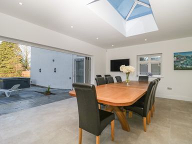 A dining room with a wooden table and black chairs under a skylight and open to an outdoor patio at Greenlawns in Burnham-On-Sea