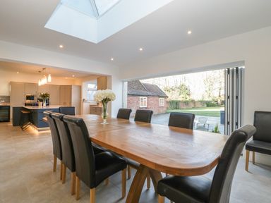 Dining area with wooden table and black chairs next to open folding doors showing outdoor space at Greenlawns in Burnham-On-Sea