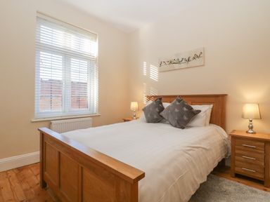 A bedroom with a wooden bed and bedside tables with lamps near a window with blinds at Greenlawns in Burnham-On-Sea