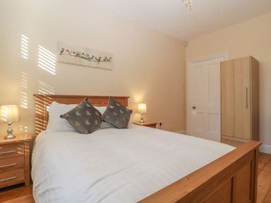 A bedroom with a wooden bed and two pillows two bedside tables with lamps a wooden wardrobe and a door at Greenlawns in Burnham-On-Sea