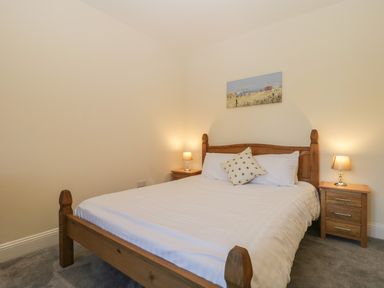 A bedroom with a wooden bed white bedding two bedside tables with lamps and a painting above the bed at Greenlawns Burnham-On-Sea