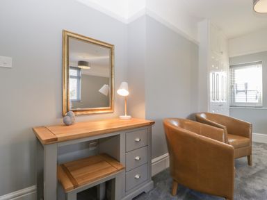 A room with a wooden desk and mirror above it with a small lamp and decoration and two brown leather chairs at Greenlawns in Burnham-On-Sea