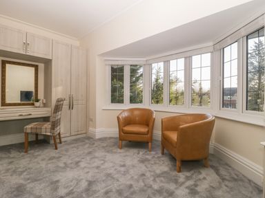 A room with two brown chairs next to windows and a built-in desk with a chair and mirror at Greenlawns in Burnham-On-Sea