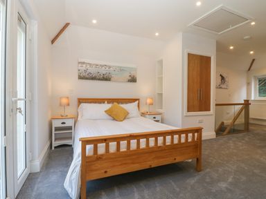 A bedroom with a wooden bed with white bedding a yellow cushion two bedside tables with lamps a painting above the bed and a staircase with a glass railing at Greenlawns Burnham-On-Sea