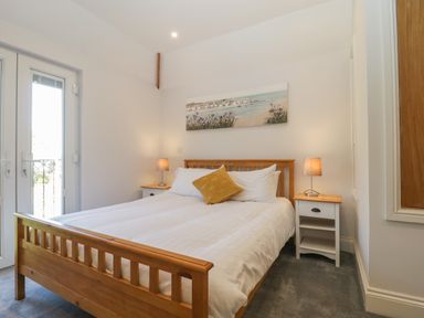 A bedroom with a wooden double bed white bedding bedside tables with lamps and a painting above the bed at Greenlawns in Burnham-On-Sea